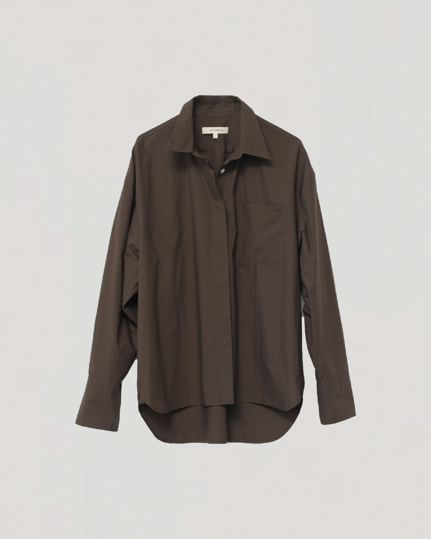 Mørkebrun oversize skjorte med krave og venstre brystlomme, hængende mod en enkel baggrund.
